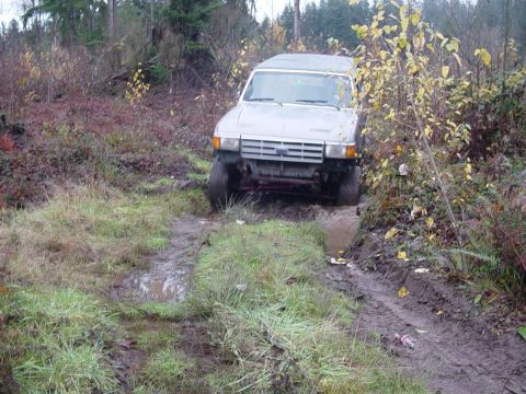 1987 Ford Bronco - 1987 Ford Bronco navigating a challenging muddy off-road path.