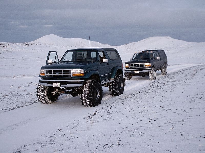 Two lifted Ford Broncos on oversized tires in snowy terrain