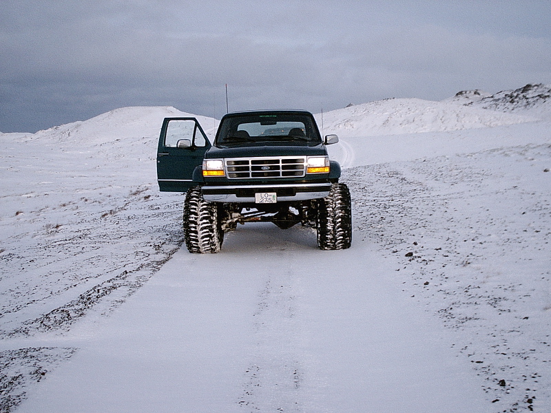 Front view of dark green lifted Ford truck on big off-road tires in snow, door open