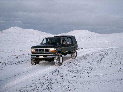 1996 Ford Bronco - A dark gray Ford Bronco with a camper shell navigates a snowy landscape under a cloudy sky.