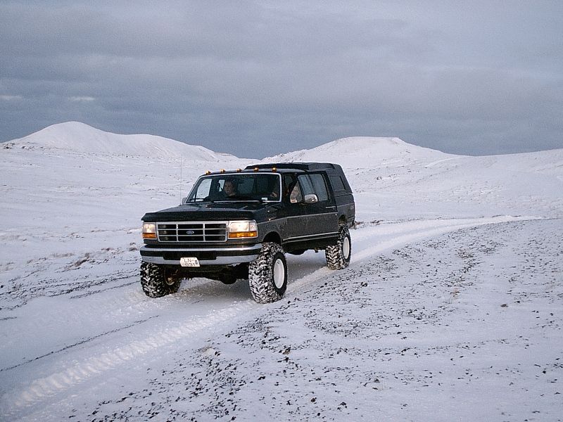 Lifted dark Ford SUV on big tires driving through snowy hilly terrain