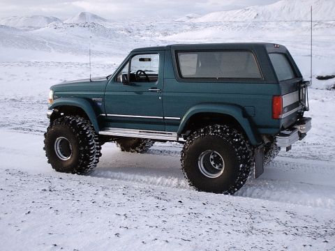 1996 Ford Bronco - 1996 Ford Bronco with large off-road tires navigates a snow-covered terrain.