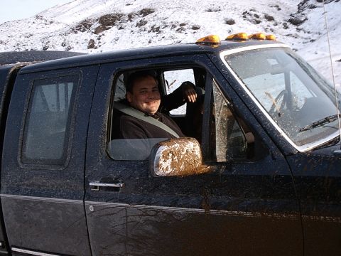 1996 Ford Bronco - A man smiles from the driver's seat of a muddy black pickup truck with amber cab lights.