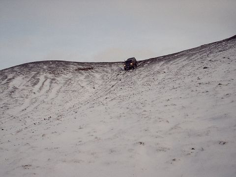 1996 Ford Bronco - A dark SUV navigates a steep, snow-covered slope under an overcast sky.