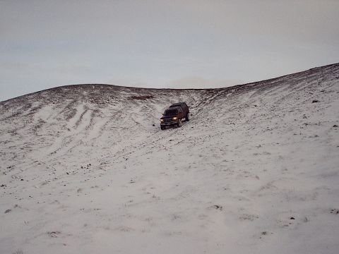 1996 Ford Bronco - A dark-colored SUV navigates a steep, snow-covered incline under an overcast sky.