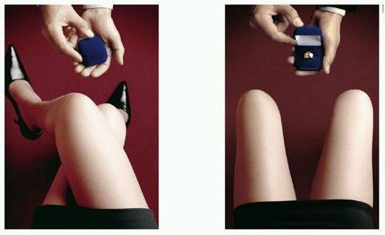 Hands hold open jewelry boxes, one with a ring, over a person's legs