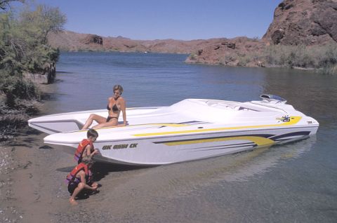 1991 Ford Bronco - A speed boat rests on the shore of a lake with two children and a woman nearby.