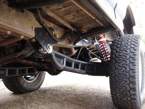 1987 Ford Bronco - The undercarriage of a modified off-road vehicle shows extensive aftermarket suspension modifications.