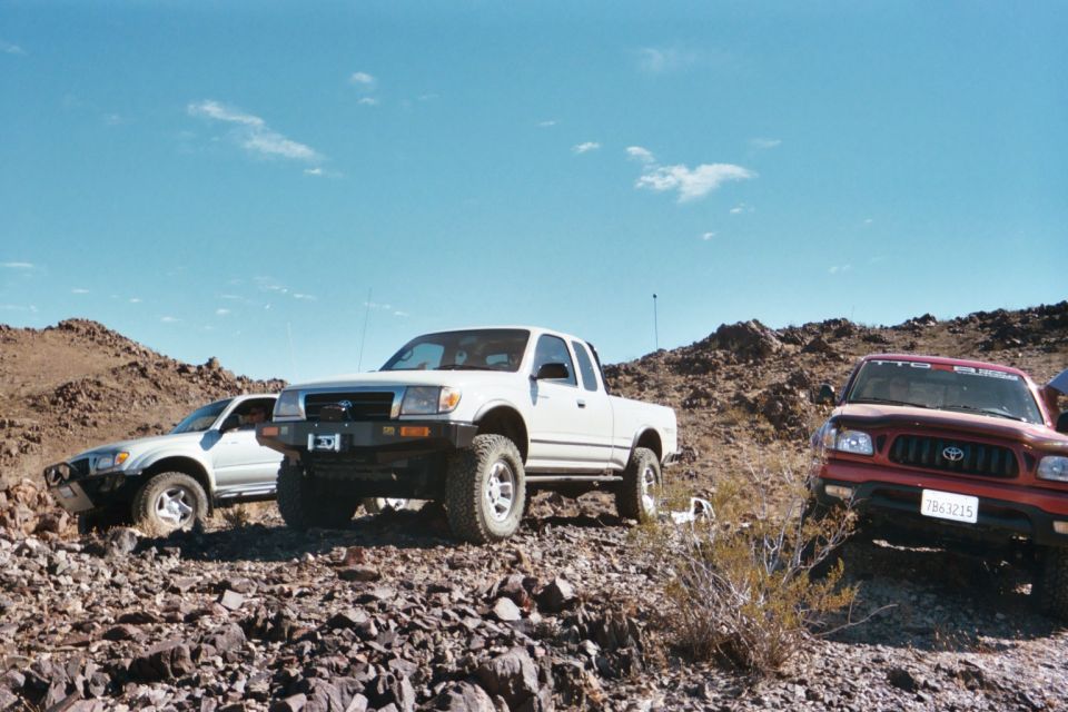 White Toyota Tacoma truck parked on rocky terrain, with a red Toyota Tacoma and a silver SUV nearby