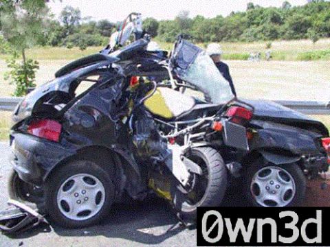 1985 Ford Bronco - Severely wrecked dark-colored small car photographed from the side at a roadside guardrail, the body torn nearly in half with the roof cut…