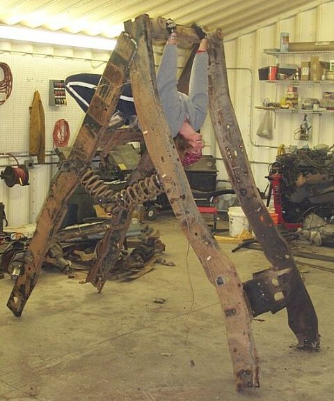 1990 Ford Bronco - A person is suspended from a large, rusty metal frame in a cluttered garage or workshop.