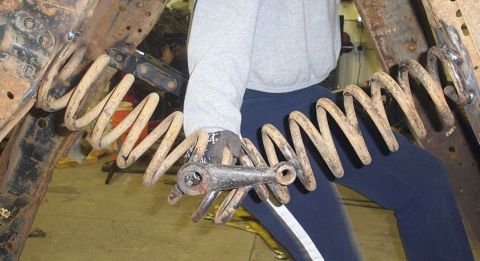 1990 Ford Bronco - Close-up of a rusty suspension coil spring and control arm being held, likely during a vehicle repair or restoration.