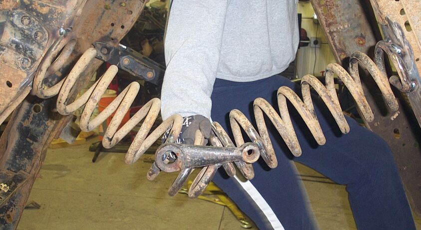 Person holding coil springs and a track bar between rusty truck frame rails