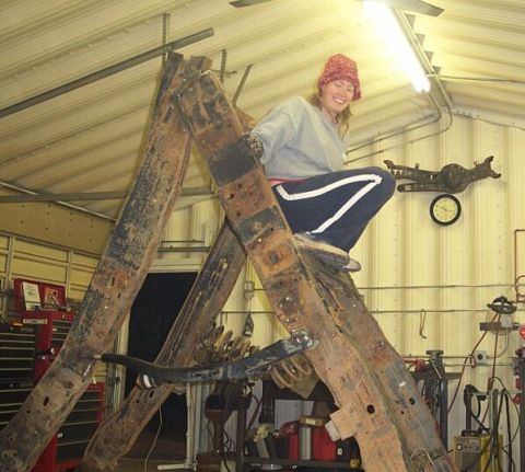1990 Ford Bronco - A person sits atop a large, rusty metal frame in a workshop, with tools and vehicle parts visible in the background.