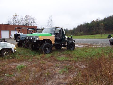 1978 Ford Bronco - Modified 1978 Ford Bronco with custom roll cage and green hood sits in a muddy field with other vehicles.