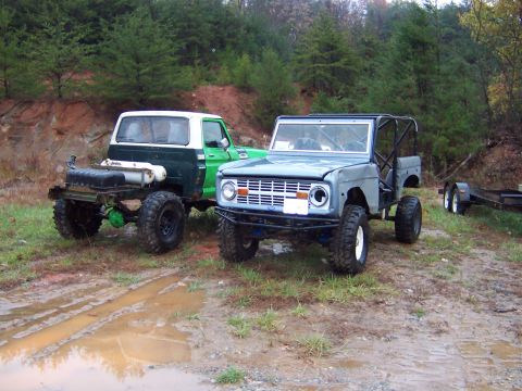 1978 Ford Bronco - A blue 1978 Ford Bronco and a green and white pickup truck sit parked in a muddy, wooded area.