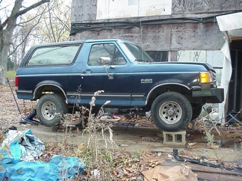 1988 Ford Bronco - This blue Ford F-150 Bronco is elevated on cinder blocks, showing its side profile and F-150 badging.