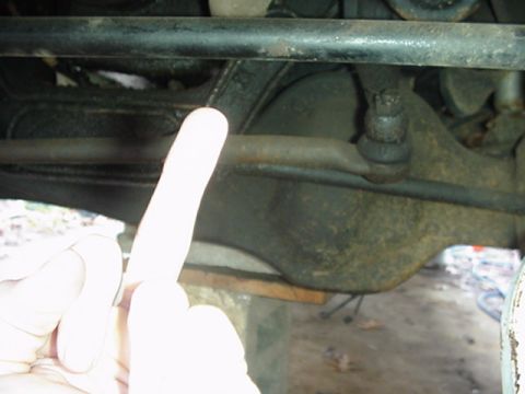 1988 Ford Bronco - Close-up of rusty steering linkage with a gloved hand pointing to it.