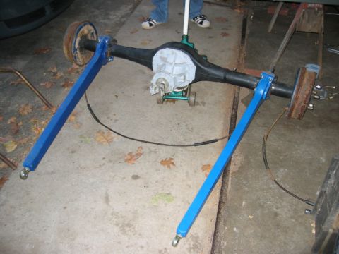 1978 Ford Bronco - A rear axle assembly on a garage floor with its black-painted housing, white-painted third member/pumpkin, rusty brake drums at both ends a…
