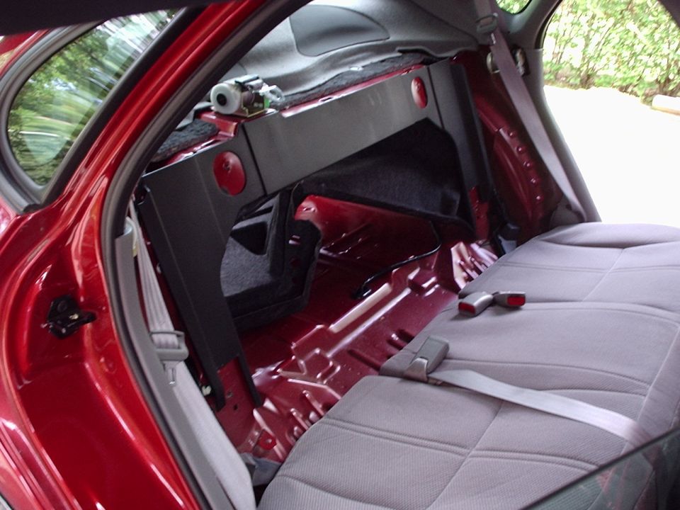 Interior of red car with rear seats removed, showing exposed metal floor and wiring