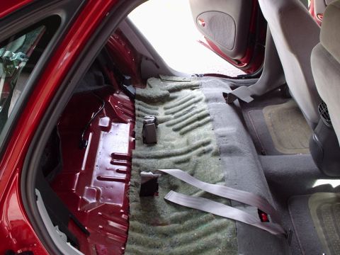 1998 Ford Taurus - The rear interior of a car is shown with the carpet removed, revealing the floor pan and seatbelt anchors.