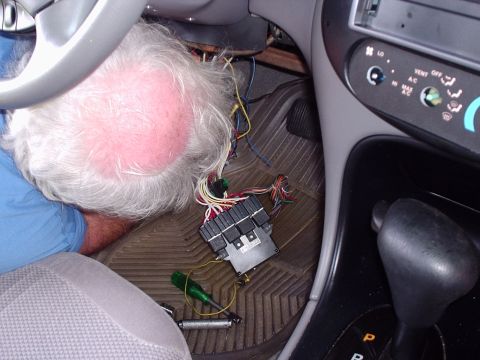 1998 Ford Taurus - A gray-haired man in a blue shirt leans under the dash of a car working on wiring, with a multi-relay junction/fuse module and its bundled…
