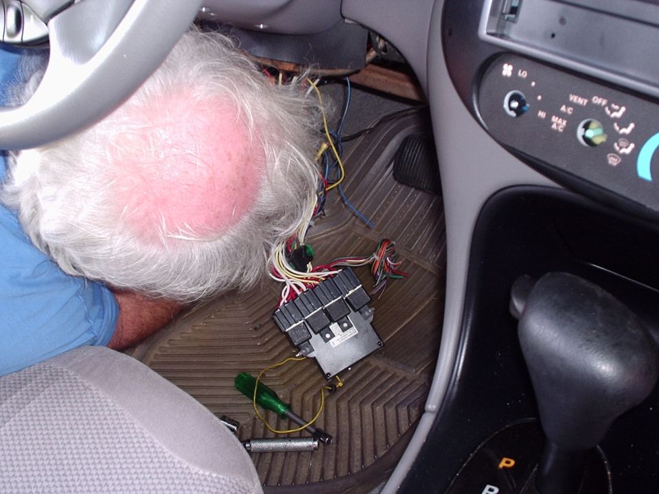 Man working under a car dash with relay module and wiring harness on the floor mat