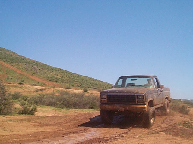Muddy black Ford pickup climbing a dirt hillside trail