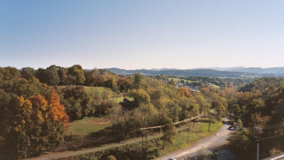 View of a rural landscape with rolling hills and trees in autumn colors. A road winds through the scene with a couple of cars visible
