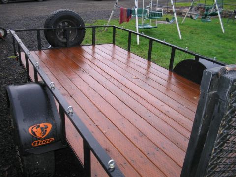 1991 Ford Bronco - A trailer with a wooden deck and a spare tire is parked in a grassy area with a swing set in the background.