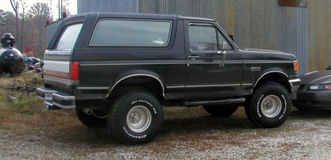 1988 Ford Bronco - This black Ford Bronco SUV is seen from the side, parked on a gravel surface.