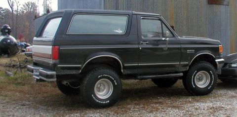 1988 Ford Bronco - This black Ford Bronco is parked on a gravel lot next to a metal building.