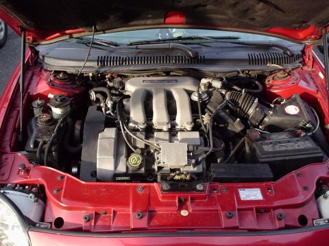 1998 Ford Taurus - Engine bay of a red car with the hood up, showing a transverse V6 with a silver 24-valve intake manifold, black plastic ducting to the air…