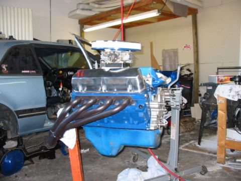 1985 Ford LTD Crown Victoria - A blue V8 engine is being worked on in a garage, with a car in the background.