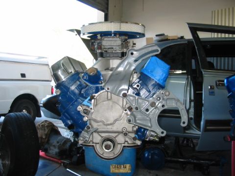 1985 Ford LTD Crown Victoria - Engine assembly in a garage, with parts of a white truck and a light blue car visible.