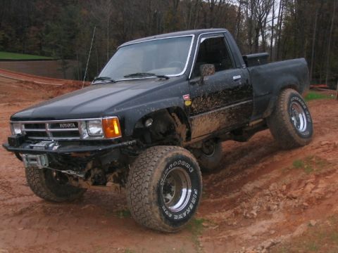 1986 Ford F-150 - This lifted Toyota pickup truck is shown navigating a muddy off-road course, its aggressive tires kicking up dirt.