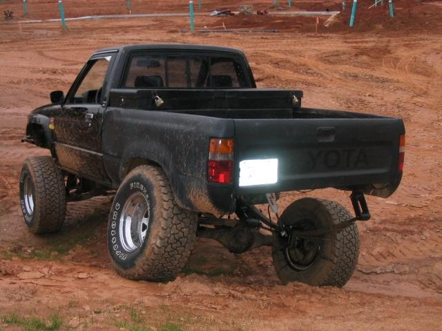 black Toyota pickup truck with lifted suspension and off-road tires, rear view