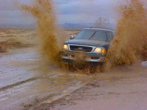 1997 Ford Expedition - A 1997 Ford Expedition navigates a muddy obstacle, sending brown water and dirt flying.