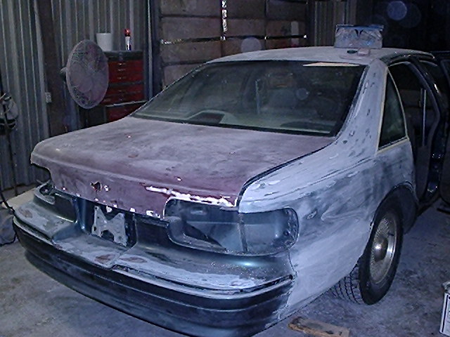 Sedan in garage with primer patches and stripped body panels during bodywork