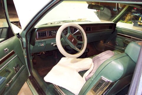 1985 Ford Crown Victoria LTD - Interior view of a green car, a white steering wheel cover and plush seat covers.