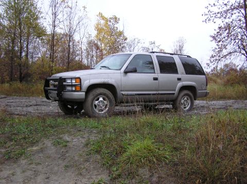 2000 Chevrolet Tahoe - A silver SUV is parked on a muddy road surrounded by trees in autumn.