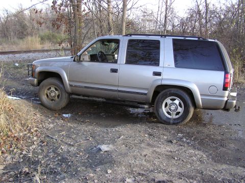 2000 Chevrolet Tahoe - This silver SUV is navigating a muddy, off-road path with trees and railroad tracks in the background.