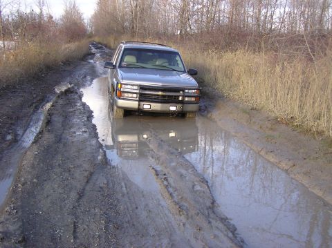 2000 Chevrolet Tahoe - This silver SUV navigates a muddy track, its grille clearly visible as it drives through deep puddles.