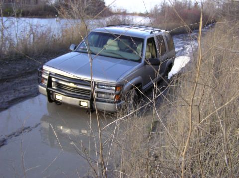 2000 Chevrolet Tahoe - A silver SUV navigates through a muddy terrain, its front tires submerged in water.