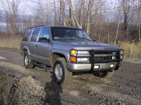 2000 Chevrolet Tahoe - This gray SUV, likely a 1995 model, is equipped with a black bull bar and is driving on a muddy dirt road.