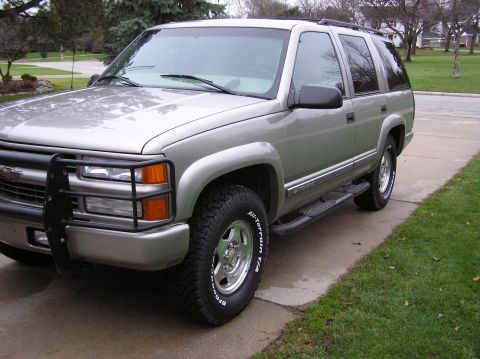 2000 Chevrolet Tahoe - This SUV is parked on a driveway with grass and trees in the background. The tires have 'All-Terrain T/A' written on them.