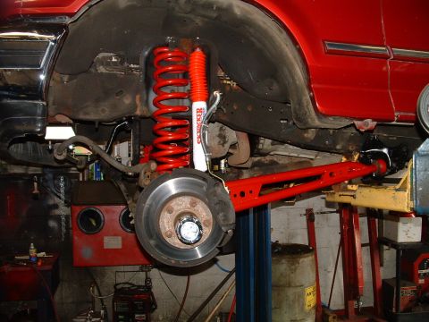 1994 Ford Bronco - Custom red suspension components are installed on the rear axle of a vehicle undergoing modifications.