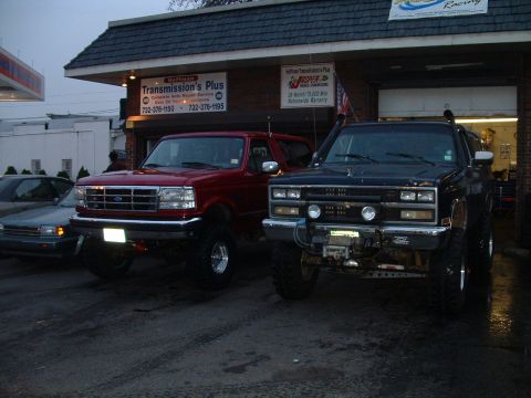 1994 Ford Bronco - A red 1994 Ford Bronco and a black Chevrolet K5 Blazer are parked outside a transmission shop.