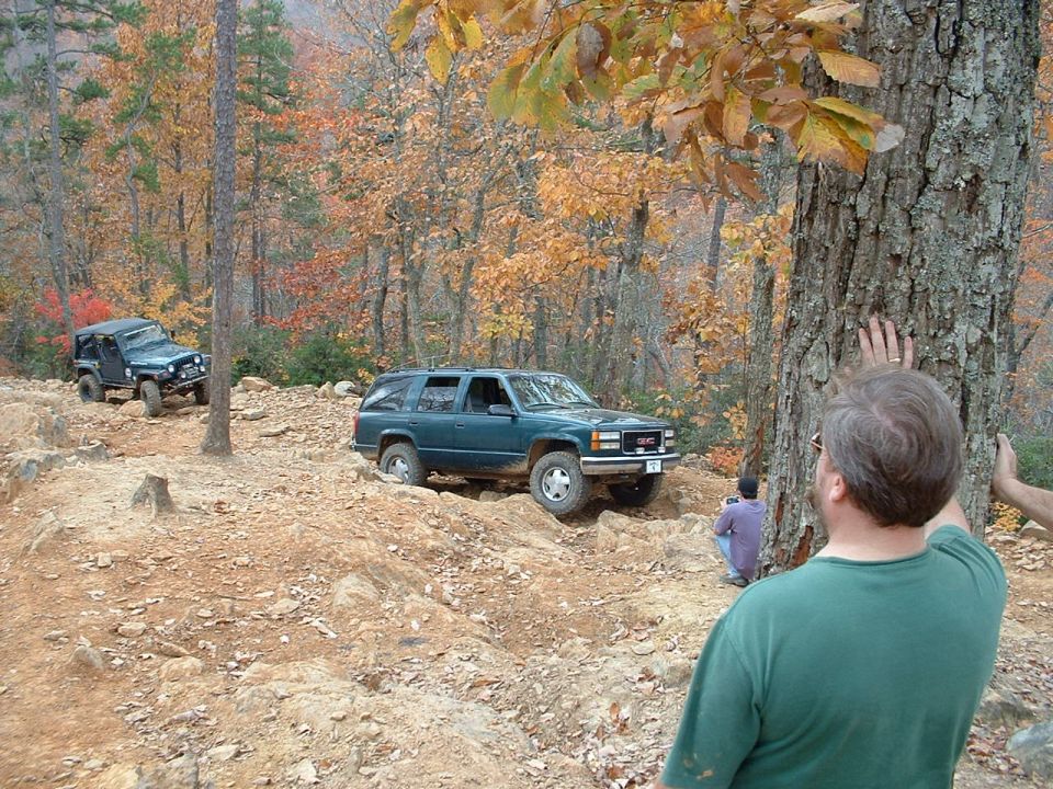 Dark green GMC Yukon descending a rocky trail with a Jeep Wrangler behind it in autumn woods
