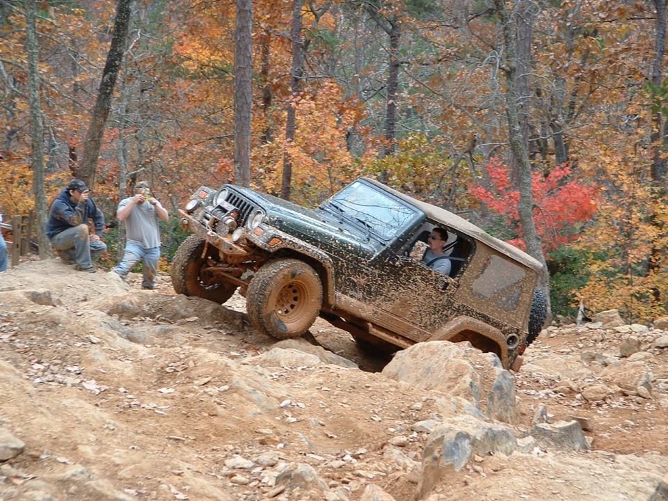 Mud-covered green Jeep Wrangler dropping into a rock hole on a fall trail run